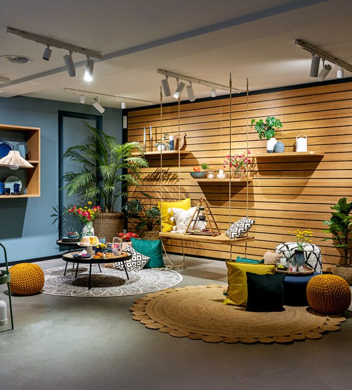 Modernes Raum mit Akzentwänden aus Holz, Zimmerpflanzen, einem Schaukelsitz, runden Teppichen, bunten Kissen und dekorativen Regalen mit verschiedenen Wohnaccessoires. Helle, gemütliche Atmosphäre.